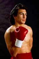 Formal portrait of Ray Mancini, shirtless with red boxing trunks and gloves.